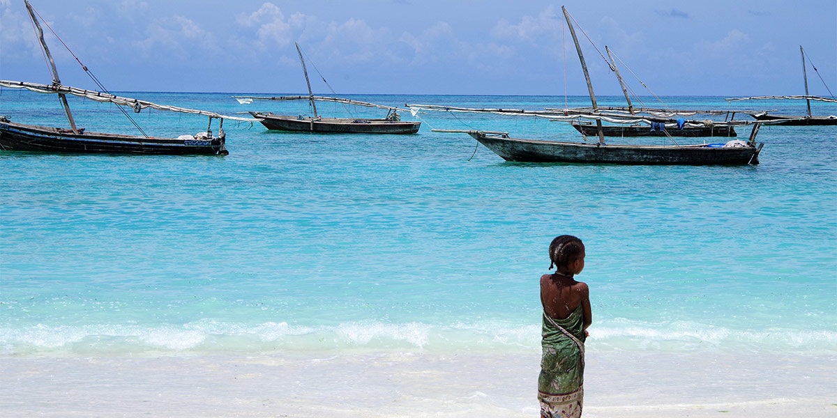 Plage de Zanzibar avec une fillette en premier plan et des bateaux de pécheurs